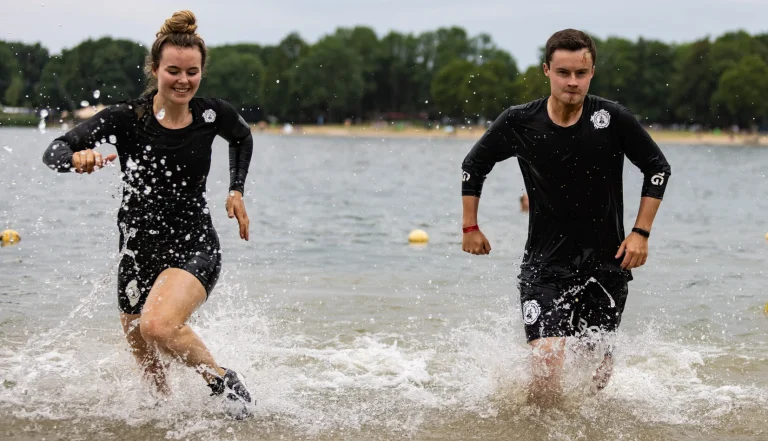 Man en vrouw die door het water heen rennen in obstacle run kleding. Ze dragen een korte obstacle run broek en een shirt met lange mouwen. De kleding is van Bjorn Borg en er staat een Strong Viking logo op.